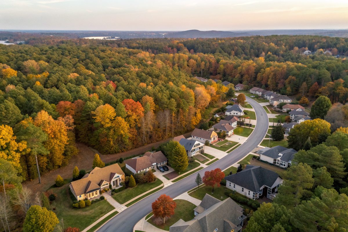 Aerial view of shingle roofs along winding streets in an autumn hardwood forest